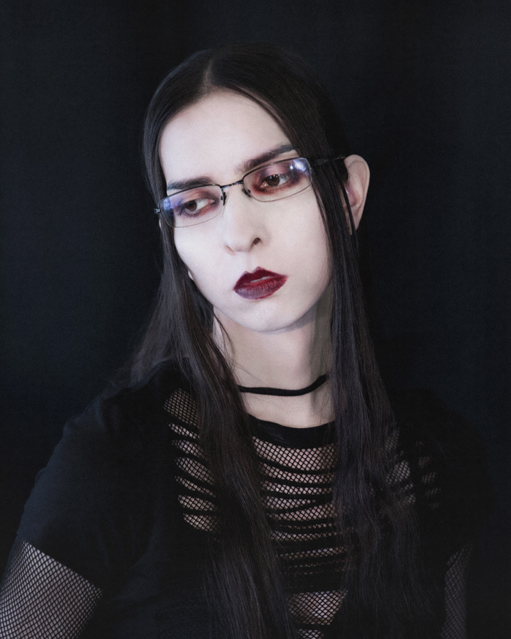 Portrait of a female model with pale skin and bruise colored eye and lip makeup against a dark backdrop